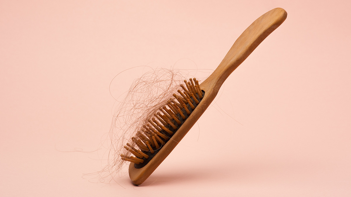 Wooden hair brush with a lot of fallen-out hair on a pink background